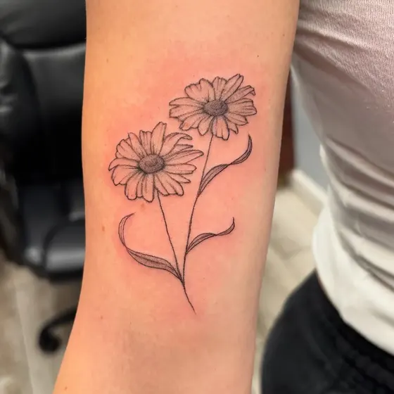 Fine line tattoo of daisies and small flowers on a client's forearm, tattooed at TBA Tattoos