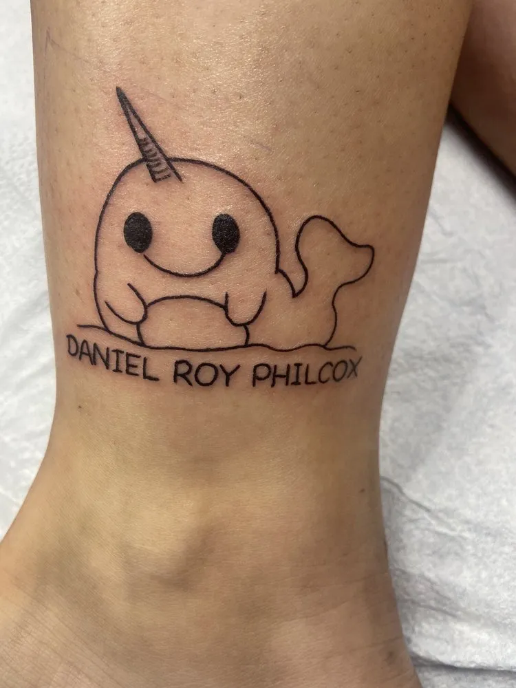 Fine line tattoo of a narwhal with a name in script on a client's ankle, tattooed at TBA Tattoos in West Palm Beach