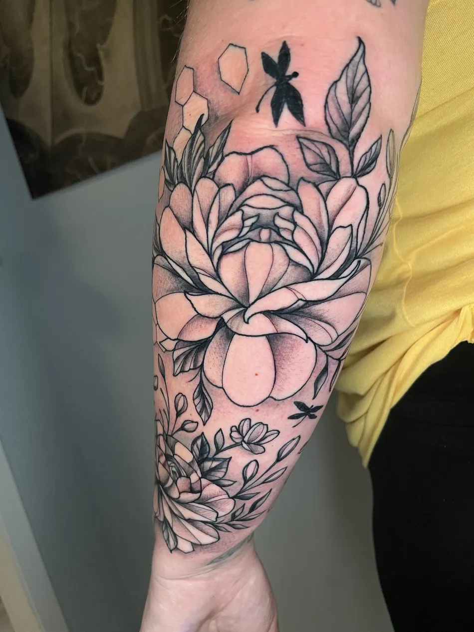 Black and grey tattoo of peonies and dragonflies wrapping a client's forearm, tattooed at TBA Tattoos in West Palm Beach