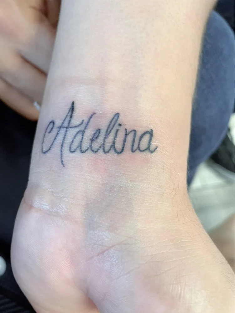 Script lettering tattoo reading Adelina with a small heart on a client's wrist, tattooed at TBA Tattoos in West Palm Beach