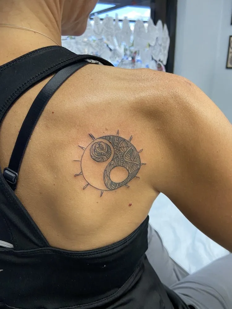 Blackwork yin yang tattoo with fine line rays on a client's shoulder blade, tattooed at TBA Tattoos in West Palm Beach